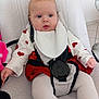 baby, baby_seat, bib, child, cute, expression, floor_tiles, heart_pattern, human, indoor, infant, looking_away, person, red_clothing, safety_harness, seat, soft_texture, tights, white_clothing, young_child