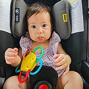 Anastasia is registered to the contest to win money with this photo: baby, car_seat, toy, purple_clothing, child, infant, seatbelt, playful, wide_eyes, tongue_out, sitting, safety, colorful_toy, indoors, cute, expression, person, young_child, child_seat, secure