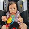 baby, car_seat, toy, purple_clothing, child, infant, seatbelt, playful, wide_eyes, tongue_out, sitting, safety, colorful_toy, indoors, cute, expression, person, young_child, child_seat, secure