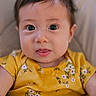 baby, child, face, portrait, yellow_clothing, floral_pattern, toy, colorful, cute, infant, closeup, expression, smile, skin, hair, eyes, indoors, soft_light, cozy, happy