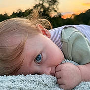 Zachery is registered to the contest to win money with this photo: child, toddler, baby, portrait, blue_eyes, blond_hair, lying_down, blanket, outdoor, sunset, soft_light, close_up, face, eye, hand, clothing, green_shirt, cozy, relaxed, nature
