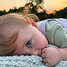 child, toddler, baby, portrait, blue_eyes, blond_hair, lying_down, blanket, outdoor, sunset, soft_light, close_up, face, eye, hand, clothing, green_shirt, cozy, relaxed, nature