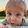 baby, child, infant, portrait, face, blue_eyes, blonde_hair, curious, surprised, outdoors, sunset, landscape, field, grass, blanket, crawling, lying_down, close_up, soft_lighting, smiling