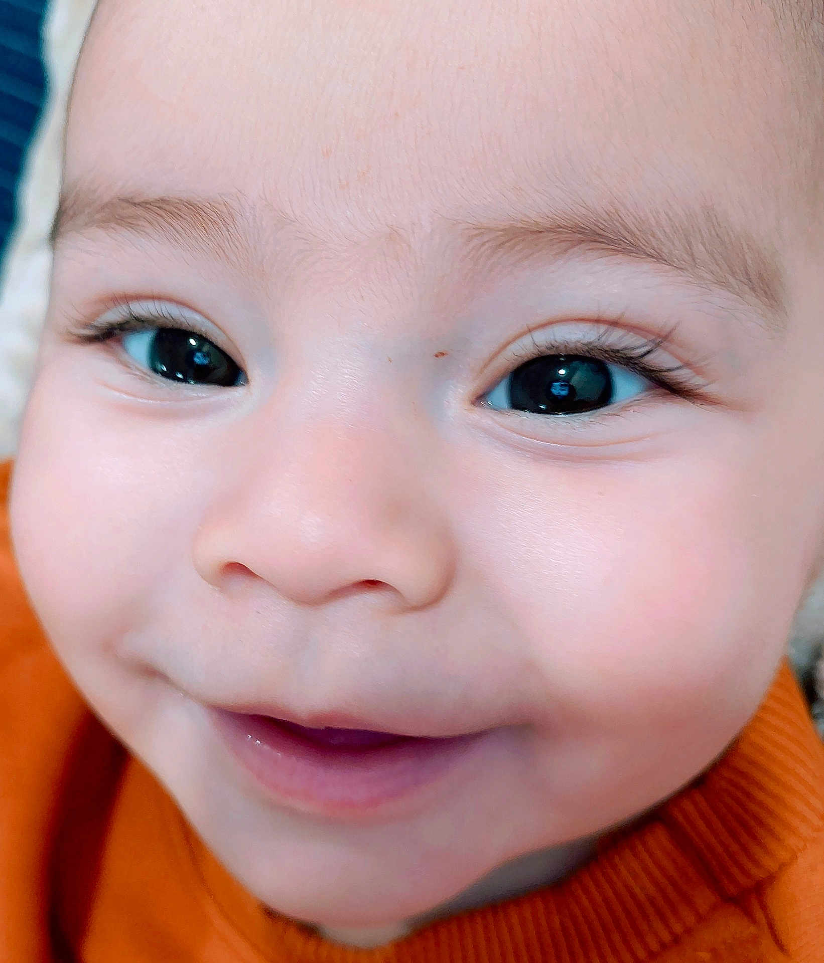Eliam is registered to the contest to win money with this photo: baby, close_up, face, smile, child, eyelashes, cheeks, skin, orange_sweater, joyful, innocence, cute, portrait, happy, young, infant, cute_expression, bright_eyes, human, childhood