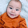 Eliam is registered to the contest to win money with this photo: baby, smiling, face, closeup, orange_sweater, bear_patch, blanket, cute, child, infant, happy, portrait, soft_texture, clothing, head, eyes, skin, warm, cozy, lying_down