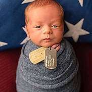 Danny joined the competition — help win amazing prizes! newborn, baby, swaddle, blue, dog_tags, portrait, face, infant, pillow, stars, knitted, wrapped, serious_expression, closeup, indoor, soft_light, red_background, cute, child, person