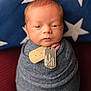 newborn, baby, swaddle, blue, dog_tags, portrait, face, infant, pillow, stars, knitted, wrapped, serious_expression, closeup, indoor, soft_light, red_background, cute, child, person