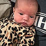 Willow is registered to the contest to win money with this photo: baby, infant, newborn, face, eyes, cheeks, leopard_print, onesie, pattern, blanket, lap, caregiver, person, portrait, close_up, indoor, clothing, gaze, bald_head, cozy