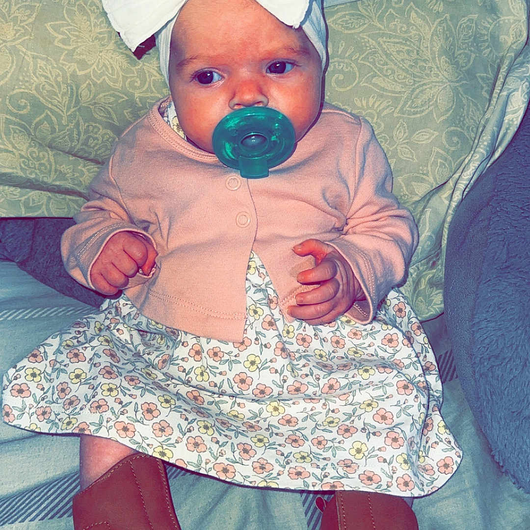 Willow is registered to the contest to win money with this photo: baby, bedding, blanket, boots, bow, cardigan, cute, fabric, feet, floral_dress, hands, headband, indoors, infant, pacifier, pattern, pillow, portrait, sitting, soft_lighting