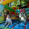 bounce_house, bunny, casual_clothing, child, colorful, daytime, easter, egg, fun, grass, inflatable, outdoor, play, recreation, smiling, socks, spring, sunlight, trees, young_child