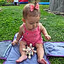 baby, child, pink_bow, pink_romper, wooden_toy, grass, blue_mat, outdoor, backyard, inflatable_play_structure, banner, summer, playtime, cute, sitting, toddler, toy, daylight, nature, fun