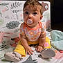 baby, pacifier, child, sitting, play_mat, colorful, floral_clothing, yellow_pants, soft_shoes, curly_hair, indoors, cute, toy, patterned_mat, innocent_look, floor_seating, small_hands, bright_colors, young_child, casual_wear