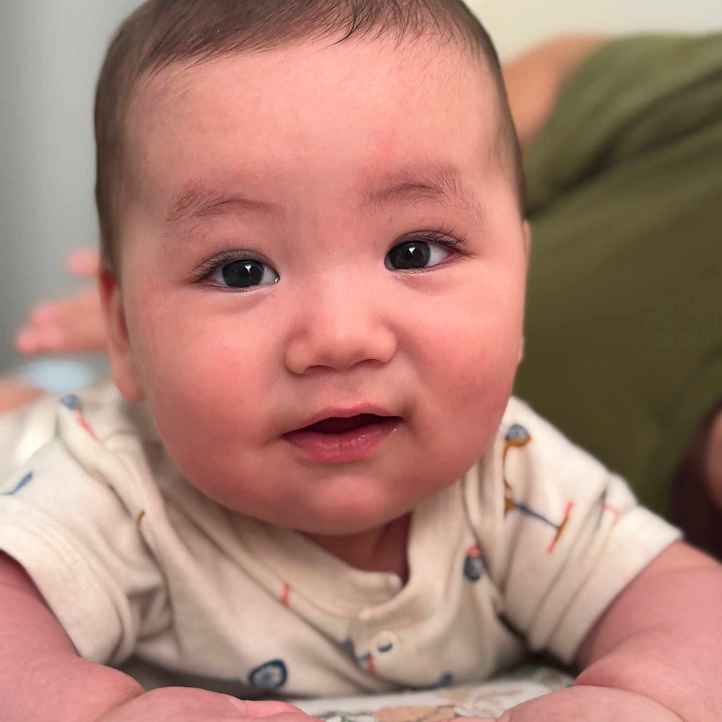 Hasan is registered to the contest to win money with this photo: baby, infant, close_up, face, hands, smile, onesie, tummy_time, curious, indoor, person, child, cute, soft_skin, young, portrait, expression, human, focus, background_blur