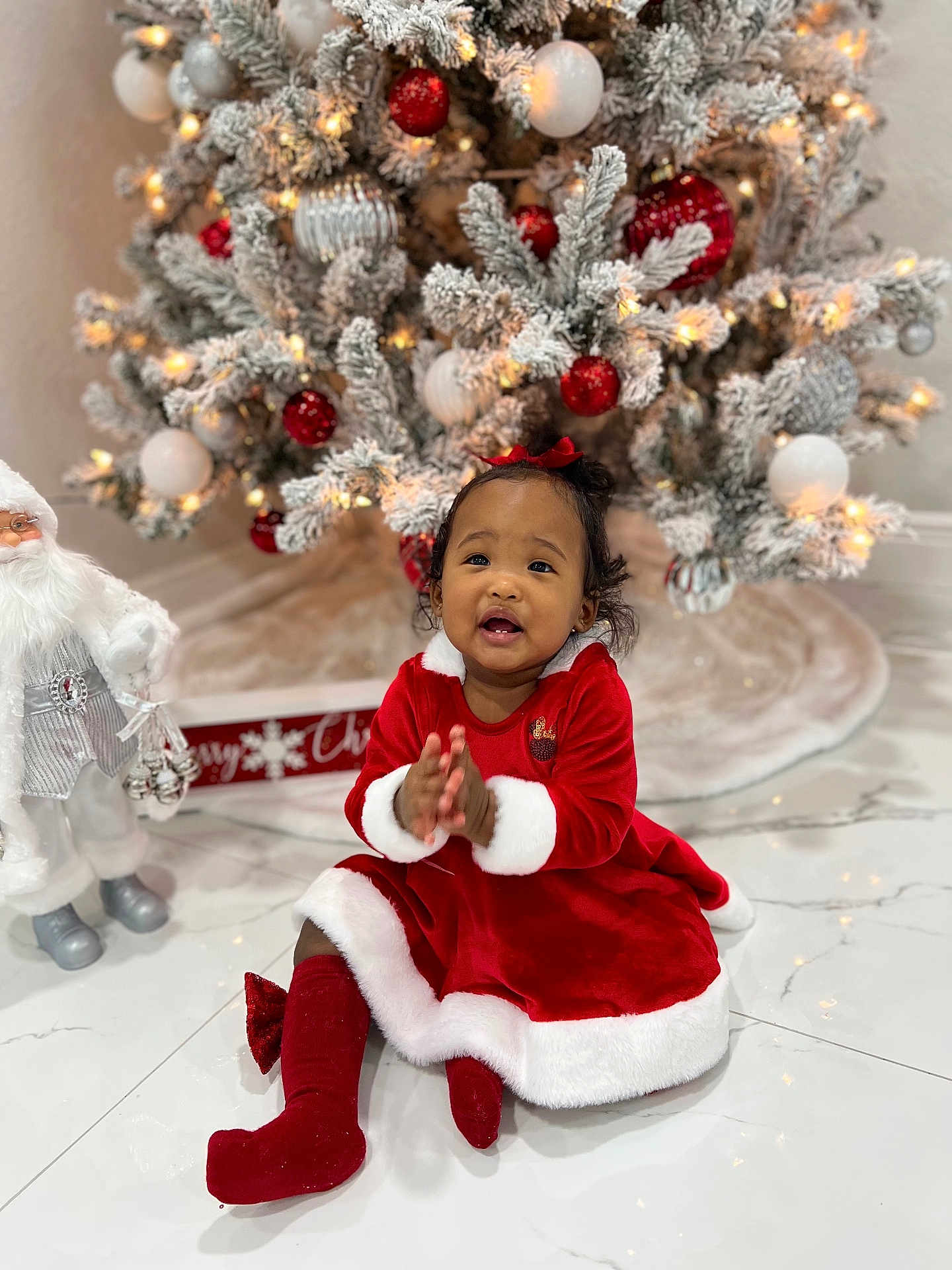 Kattleya joined the competition — help win amazing prizes! toddler, child, christmas_tree, christmas_ornaments, red_dress, festive_clothing, santa_figurine, holiday, indoor, smiling, clapping, marble_floor, decorations, red_bow, christmas_lights, white_fur_trim, cute, happy, celebration, person