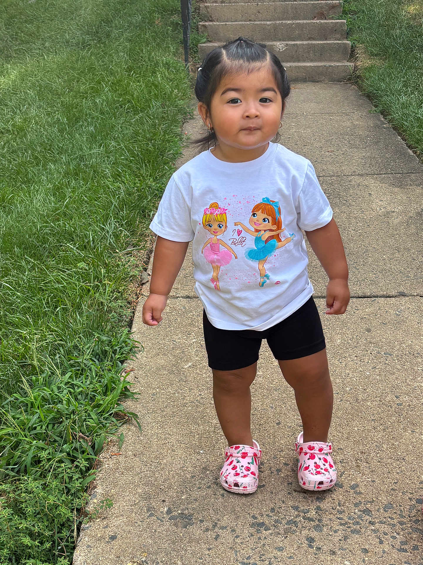 Amy joined the competition — help win amazing prizes! toddler, child, outdoor, sidewalk, grass, stairs, white_tshirt, ballerina_print, black_shorts, pink_shoes, cherry_pattern, cute, standing, person, young_child, hair_tied, earrings, summer_clothing, daylight, smiling