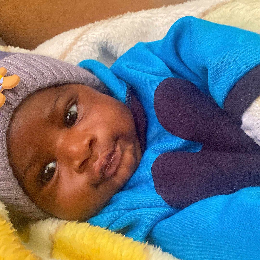 Lael joined the competition — help win amazing prizes! baby, bear_decoration, blanket, blue_clothing, child, cozy, cute, expression, face, fluffy, hat, indoor, infant, knitted_hat, lying_down, mittens, portrait, warm_clothing, white_blanket, yellow_blanket