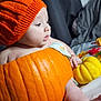 baby, pumpkin, orange_hat, autumn_leaves, pine_cones, small_pumpkins, fall_decor, baby_in_pumpkin, knitted_hat, cute, festive, holiday, seasonal, indoor, portrait, child, table_decor, soft_lighting, costume, celebration
