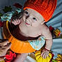 baby, pumpkin, orange_hat, autumn_leaves, yellow_pumpkin, white_pumpkin, pinecone, smiling, cute, child, fall_decor, seasonal, festive, costume, holiday, sitting, hand, blanket, indoors, portrait