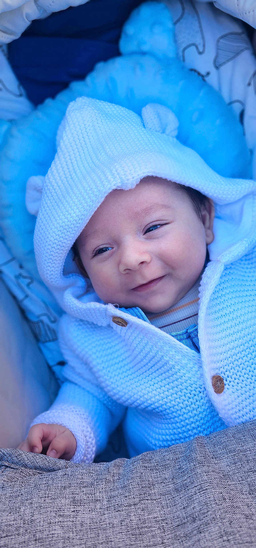 Noah joined the competition — help win amazing prizes! baby, infant, smile, knitted_hoodie, blue_blanket, cozy, cute, child, newborn, portrait, warm_clothing, soft_texture, hand, face, resting, happy, closeup, indoors, cushion, comfort