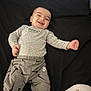 Taytum is registered to the contest to win money with this photo: baby, smiling, grey_clothing, long_sleeve, pants, teddy_bear, black_background, lying_down, happy, infant, child, person, text_on_clothing, nike_logo, patterned_pants, cute, indoor, portrait, toddler, relaxed