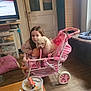 girl, dog, toy_stroller, baby_doll, indoor, wooden_floor, television, furniture, pink, child, pet, home, cabinet, curtains, cushion, bottle, table, can, lighter, floor