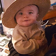 Masséo a rejoint le concours — aidez-le/la à gagner de superbes lots ! baby, child, hat, straw_hat, person, smile, indoor, striped_clothing, sweater, holding, cute, face, portrait, warm_clothing, infant, curious, hand, cozy, dim_lighting, background