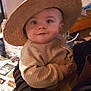 baby, child, hat, straw_hat, person, smile, indoor, striped_clothing, sweater, holding, cute, face, portrait, warm_clothing, infant, curious, hand, cozy, dim_lighting, background