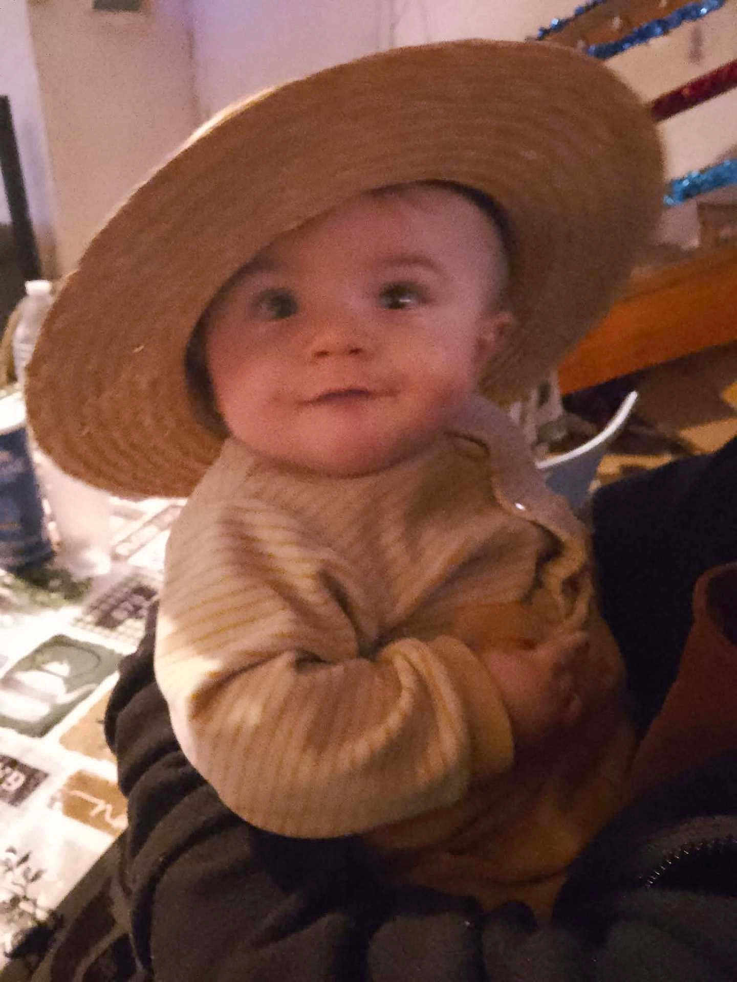 Masséo a rejoint le concours — aidez-le/la à gagner de superbes lots ! baby, child, hat, straw_hat, person, smile, indoor, striped_clothing, sweater, holding, cute, face, portrait, warm_clothing, infant, curious, hand, cozy, dim_lighting, background