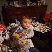 Masséo participe au concours pour gagner de l'argent avec cette photo : baby, child, toy, container, table, indoor, furniture, photograph, person, clothing, socks, face, curious, dim_light, household, decor, blanket, adult_arm, framed_picture, wooden