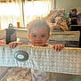 toddler, child, playpen, blanket, curtains, window, indoor, smile, face, hands, mesh, fabric, hair, room, pile_of_clothes, baby, daylight, furniture, person, home
