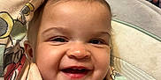 Amelia is registered to the contest to win money with this photo: baby, smiling, child, infant, face, happy, clothing, seat, cushion, indoor, person, cute, raising_hand, portrait, young, closeup, babywear, playful, expression, cozy