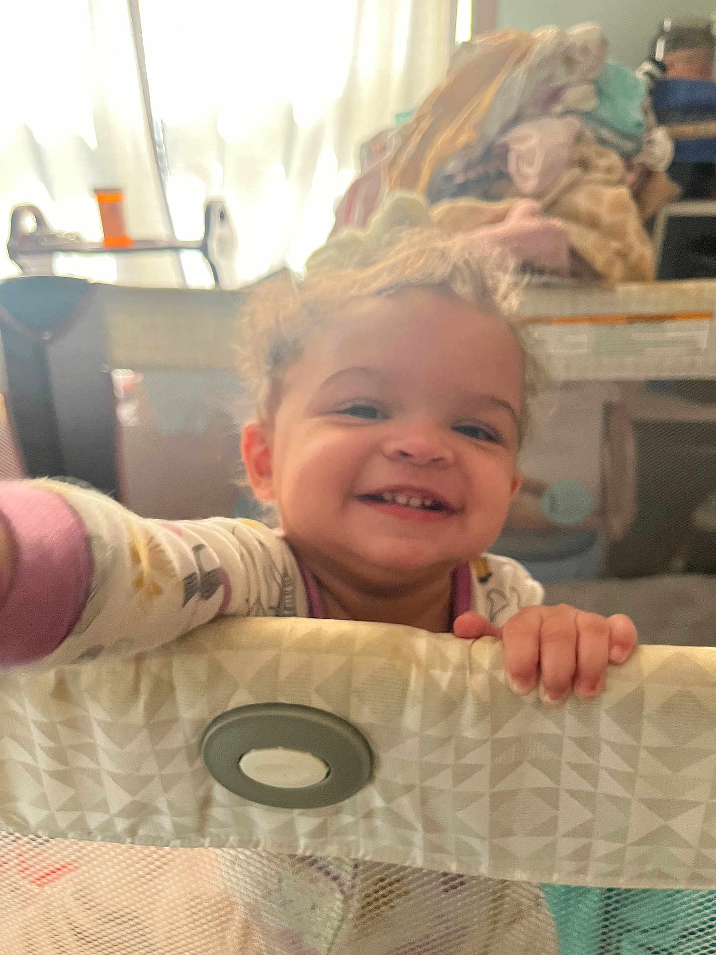 Amelia joined the competition — help win amazing prizes! toddler, child, smile, happy, playpen, pajamas, curly_hair, indoors, baby, hand, furniture, blanket, mesh, face, person, home, cozy, cute, infant, grin