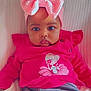 baby, child, infant, pink_bow, pink_clothing, cartoon_print, blanket, soft_texture, cute, portrait, indoors, seated, serious_expression, headband, chubby_cheeks, clothing, person, face, young_child, cozy