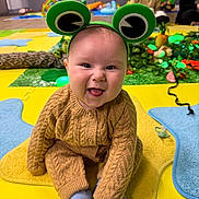 Alistair joined the competition — help win amazing prizes! baby, child, smiling, frog_headband, knitted_clothing, indoor, playmat, colorful, happy, sitting, tongue_out, adult, toy, background, people, floor, cozy, cute, portrait, fun