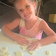Tessa a rejoint le concours — aidez-le/la à gagner de superbes lots ! casual, chair, child, dominoes, furniture, game, girl, hair, hands, happy, indoor, messy_hair, person, playing, smiling, table, tank_top, tiles, white, young