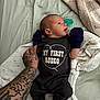 Roper is registered to the contest to win money with this photo: baby, bed, blanket, clothing, cute, fabric, foot, hand, indoor, infant, lying_down, mittens, newborn, pacifier, person, resting, skin, sleepwear, tattooed_arm, text_on_clothing