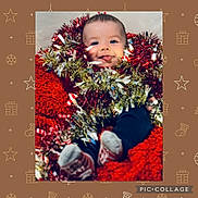 Isaiah is registered to the contest to win money with this photo: baby, tinsel, festive, holiday, red_blanket, smiling, tongue_out, cozy, cute, indoor, christmas, decorations, child, person, sock, blue_pants, face, happy, celebration, cute_expression