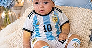 Nashly is registered to the contest to win money with this photo: argentina_jersey, baby, blanket, blue, bow, child, couch, fairy_lights, flowers, football, headband, indoors, number_10, portrait, sitting, smiling, soccer, soft_lighting, sportswear, white