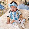 argentina_jersey, baby, blanket, blue, bow, child, couch, fairy_lights, flowers, football, headband, indoors, number_10, portrait, sitting, smiling, soccer, soft_lighting, sportswear, white