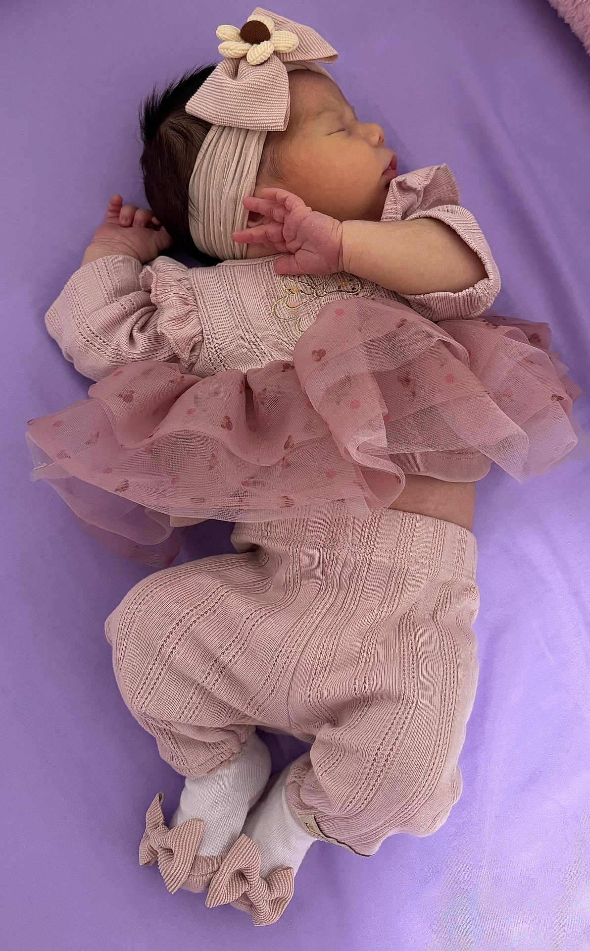 Nashly is registered to the contest to win money with this photo: baby, sleeping, infant, pink_clothing, headband, flower, ruffled_skirt, socks, bows, soft_surface, purple_background, cute, peaceful, newborn, portrait, child, hands, feet, cozy, toddler