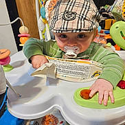 Lennox joined the competition — help win amazing prizes! baby, child, pacifier, hat, plaid, green_shirt, activity_center, toy, button, hand, face, eyes, indoor, colorful, play, infant, seat, pattern, fabric, curious