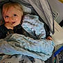 Lennox is registered to the contest to win money with this photo: baby, blanket, child, smile, face, hand, stroller, car_seat, cozy, clothing, indoor, light_hair, blue_blanket, patterned_blanket, happy, infant, cute, soft_texture, person, seated