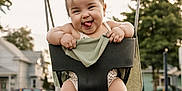 Jasmine is registered to the contest to win money with this photo: baby, child, swing, playground, outdoor, smiling, tongue_out, happy, legs, sandals, trees, houses, sidewalk, chains, clothing, green_blanket, sunset_light, face, person, fun