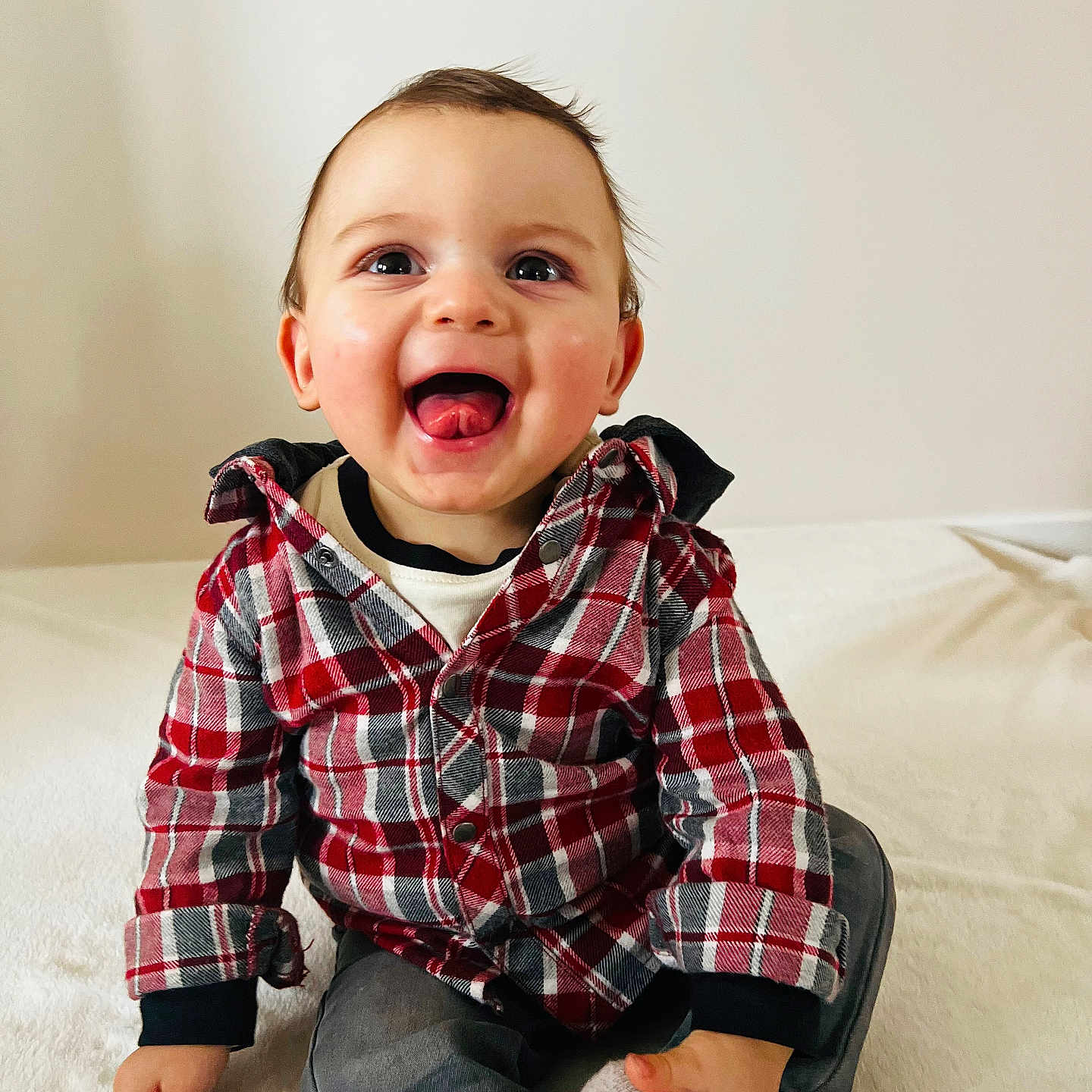 Nino a rejoint le concours — aidez-le/la à gagner de superbes lots ! baby, casual_clothing, child, cozy, cute, eyes, hands, happy, indoors, jeans, plaid_shirt, playful, portrait, red_plaid, sitting, smiling, sock, toddler, tongue_out, white_background