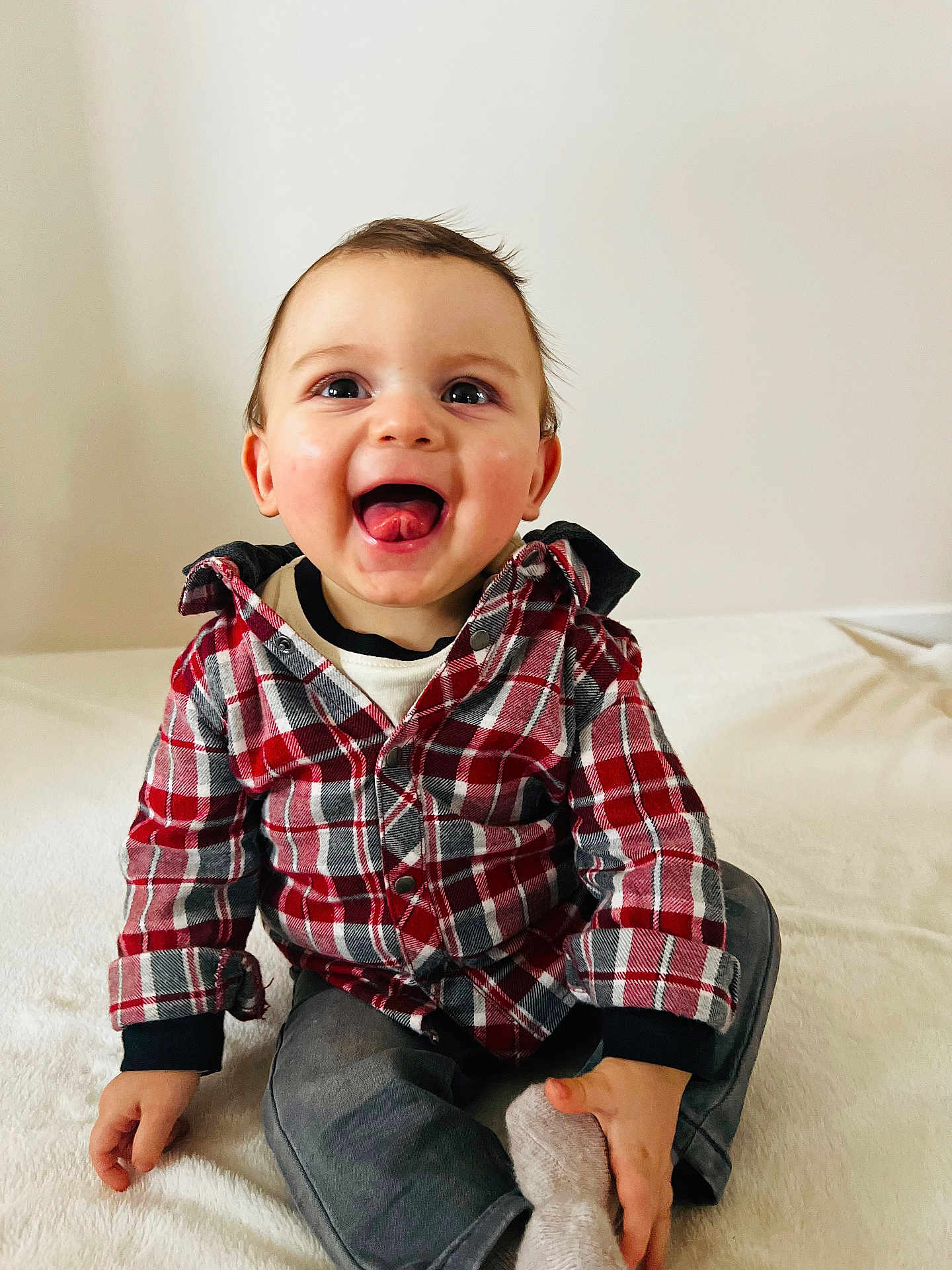 Nino a rejoint le concours — aidez-le/la à gagner de superbes lots ! child, baby, toddler, smiling, tongue_out, plaid_shirt, red_plaid, sitting, indoors, white_background, portrait, cute, happy, eyes, hands, jeans, sock, cozy, casual_clothing, playful