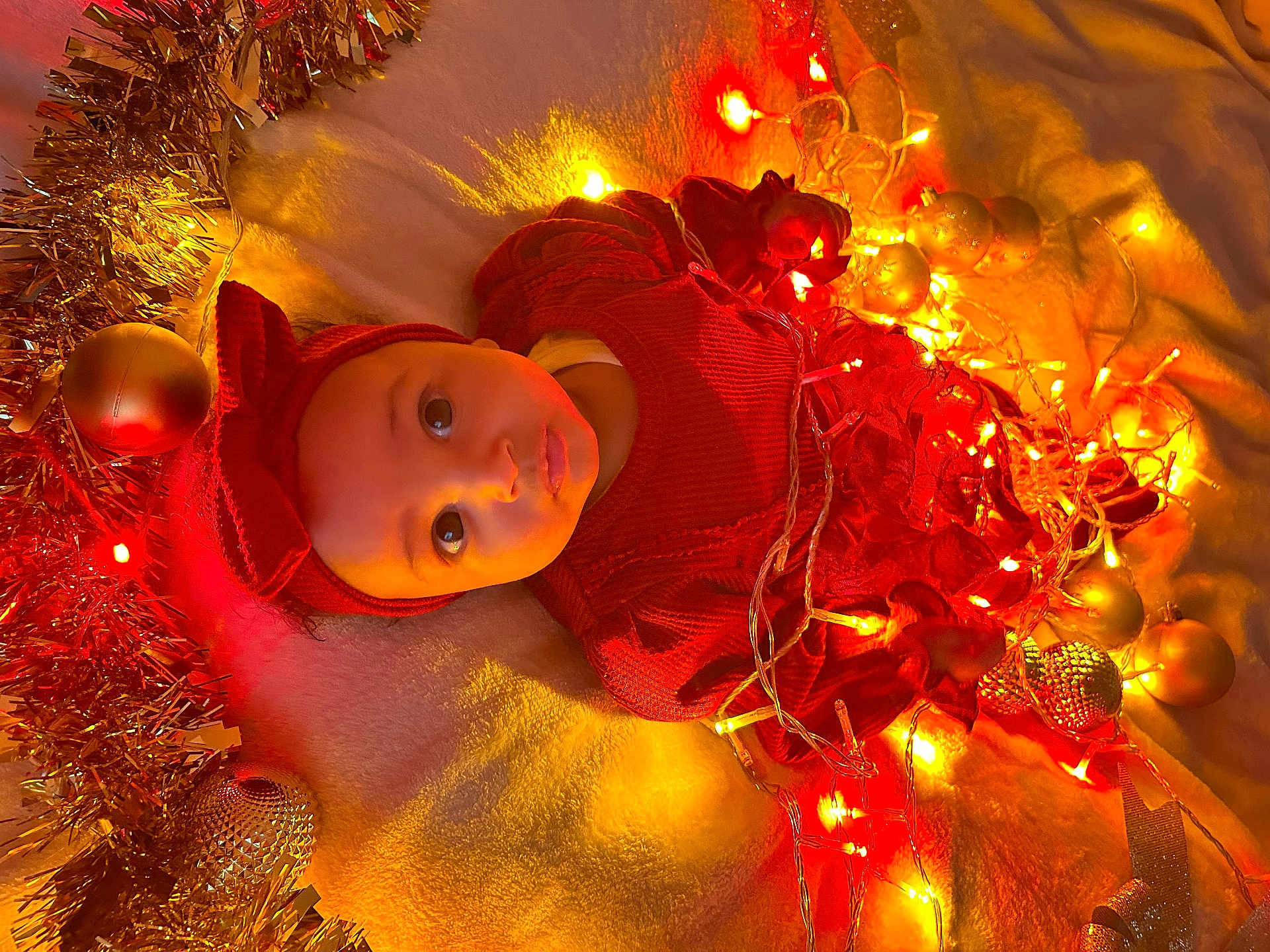 Kaysha a rejoint le concours — aidez-le/la à gagner de superbes lots ! baby, child, christmas, lights, ornaments, red_clothing, headband, festive, holiday, tinsel, blanket, cute, portrait, indoors, decorations, smile, face, infant, warm_lighting, celebration