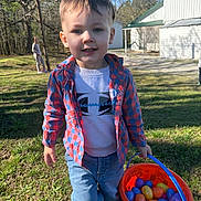Liam joined the competition — help win amazing prizes! child, boy, plaid_shirt, jeans, bucket, plastic_eggs, outdoor, grass, sunny, daylight, smile, toy, tree, building, backyard, person, casual_clothing, happy, activity, spring