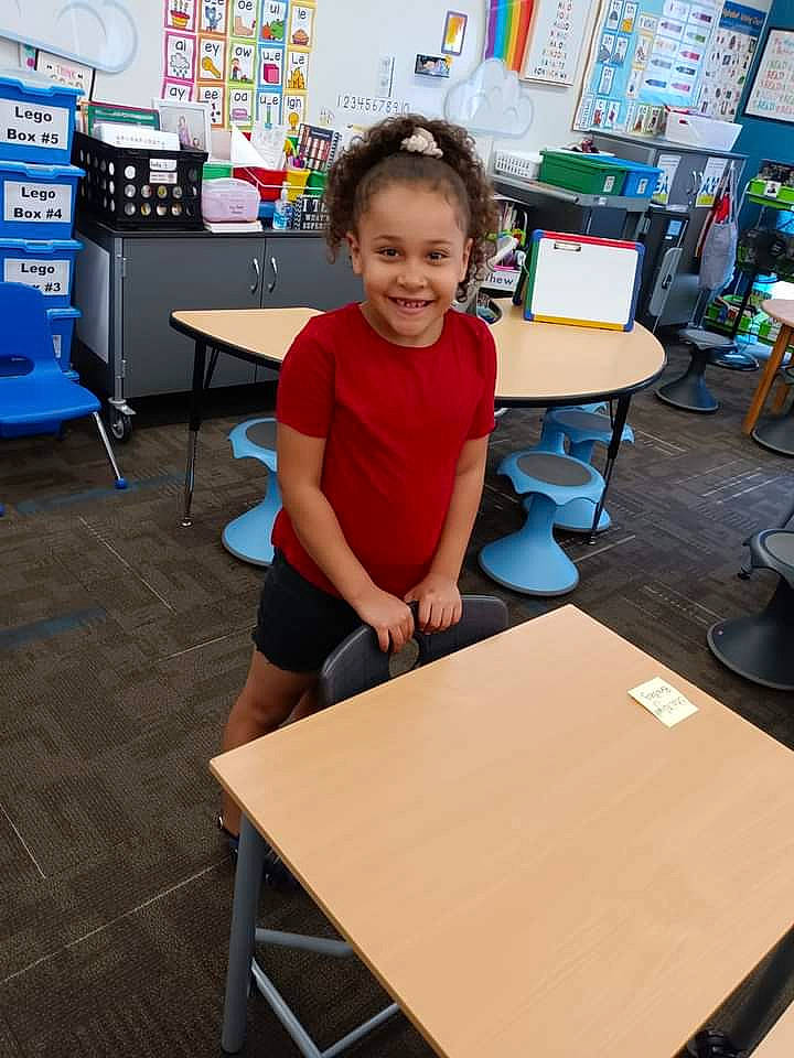 Sha'Niyah joined the competition — help win amazing prizes! chair, child, class, desk, education, engineering, fun, furniture, joy, leisure, person, play, room, sharing, shorts, smile, standing, t_shirt, table, toddler