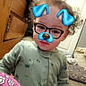 toddler, child, baby, portrait, indoor, bedroom, curly_hair, glasses, digital_filter, blue_accessories, mustache_filter, smiling, facial_expression, pajamas, green_clothing, sitting, wooden_furniture, bed, bedding, close_up