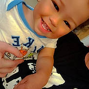 Zayden joined the competition — help win amazing prizes! child, toddler, smiling, happy, portrait, close_up, indoor, sitting, face, teeth, curly_hair, white_shirt, blue_trim, black_and_white, adult_hand, family, home, playful, camera, selfie
